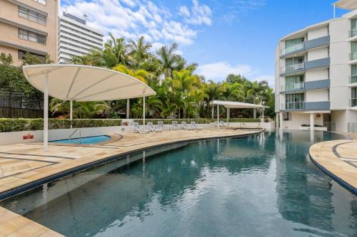 a swimming pool with chairs and an umbrella next to a building at Beachside Penthouse w Private Rooftop & Oceanviews in Caloundra