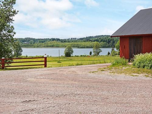 a dirt road next to a red barn and a lake at 6 person holiday home in GAMLEBY-By Traum in Gamleby