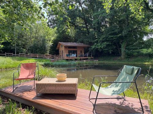 two chairs and a table on a wooden deck with a house at La cabane sur l'étang in Étival-Clairefontaine