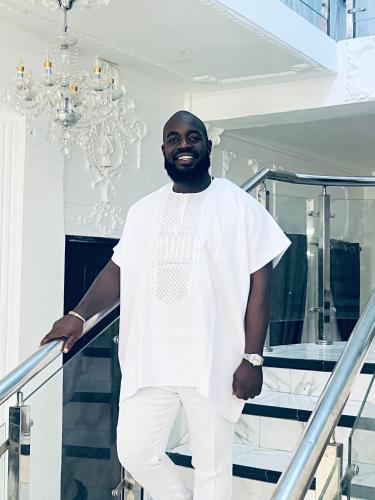 a man standing on a staircase wearing a white shirt and white pants at The Peacock Mansion in Kumasi