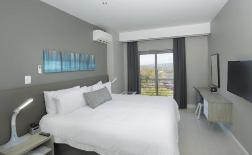 a white bedroom with a large bed and a tv at The Capital on Bath in Johannesburg