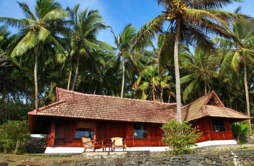 a small house with two chairs and palm trees at Niraamaya Wellness Retreats, Surya Samudra, Kovalam in Kovalam