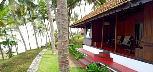 a house with a porch with chairs and palm trees at Niraamaya Wellness Retreats, Surya Samudra, Kovalam in Kovalam