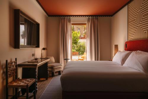 a bedroom with a bed and a desk and a window at Palacio De Godoy Caceres, Curio Collection By Hilton in Cáceres