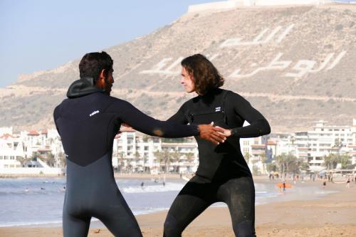 a man and woman in wet suits on the beach at Surf Treasure Morocco in Aourir