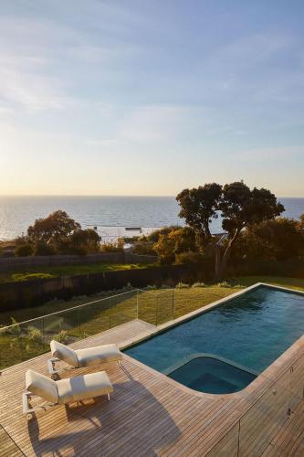 a swimming pool with two lounge chairs and the ocean at Blanc de Noir Luxe Grandeur with Pool and Spa in Mount Martha