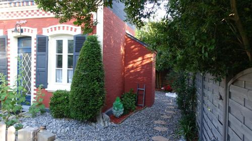 a red brick house with a red door and bushes at Gîte My Cottage Baie de Somme avec sauna in Cayeux-sur-Mer