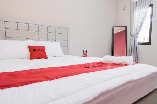a large white bed with a red blanket on it at RedDoorz Syariah near Hajimena Lampung in Lampung