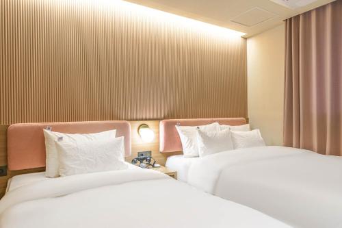 two beds in a hotel room with white pillows at Yongin IPPDA Petite in Yongin