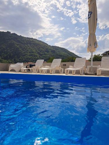 a pool with chairs and an umbrella and the water at Apartmani Sunce Stara planina in Crni Vrh
