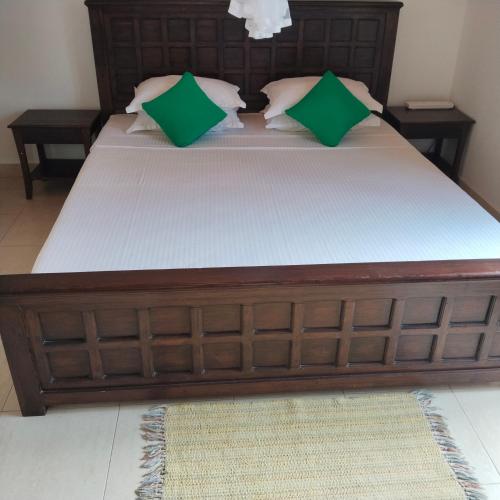a large wooden bed with green pillows on it at Tharul Home in Bentota