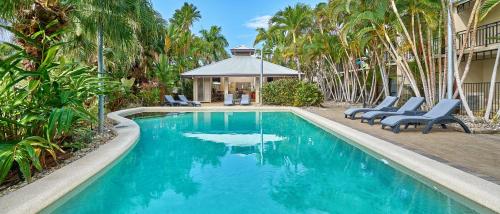 a swimming pool with chairs and a house with palm trees at Trinity Beach Club Holiday Apartments in Trinity Beach