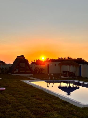 a sunset over a swimming pool with the sun setting at Maison dar jad in Chaba Remada