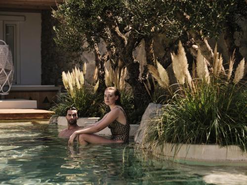 a woman and a man sitting in a swimming pool at Kove Mykonos - A Myconian Collection Hotel in Ornos
