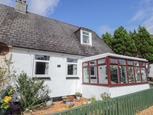 a white house with red windows and a fence at The Highlander in Dornie