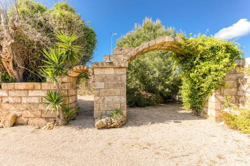 an archway in a stone wall with bushes and trees at Guest House Fontanelle in Ugento