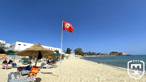 a beach with a flag and chairs and people on it at Hotel La Residence Hammamet in Hammamet