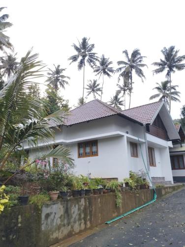 a white house with palm trees in the background at Highrange Retreat in Idukki
