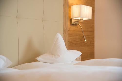 a bedroom with two beds with white sheets and a lamp at Hotel Rosskopf in Vipiteno