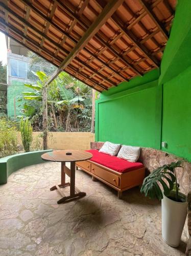a patio with a couch and a table and a green wall at Quarto para 6 a 900m da Vila do Capão in Vale do Capao