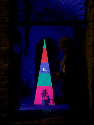 a man standing in a dark room with a colorful pyramid at La casa dell’artista di Vittorio Vertone in Pietragalla