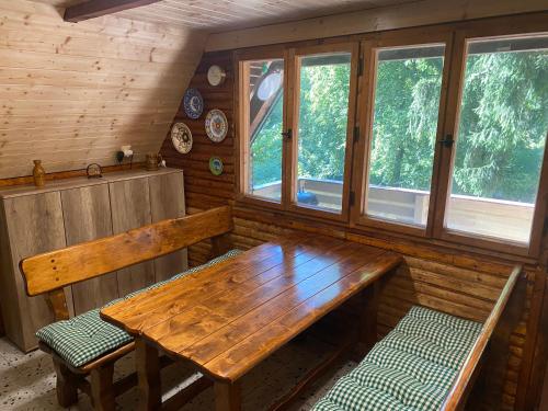 a wooden table and benches in a room with windows at Chata Roubenka in Jedovnice