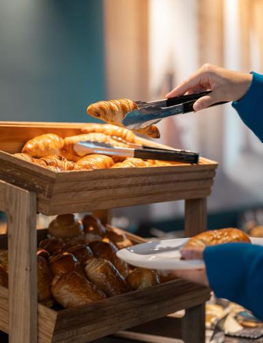 a person holding a pair of tongs over a tray of bread at Radisson Hotel Reims in Reims