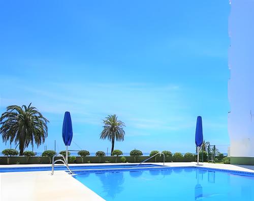 ein großer Pool mit Palmen und blauen Sonnenschirmen in der Unterkunft Modern Marina Apt Fantastic in Estepona