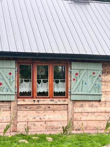 a wooden building with flowers in the windows at Rozkoszne Roztocze - domek na wynajem 