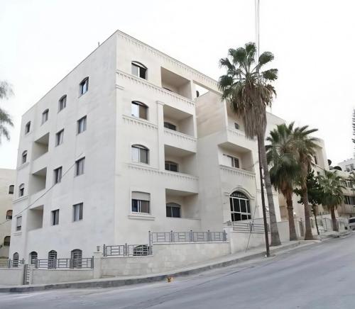 a white building with palm trees in front of it at EVANNA SUITE AND HOTELs ايفانا للشقق الفندقيه و المفروشه in Amman