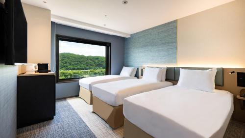two beds in a hotel room with a window at ANA Holiday Inn Iwate Kitakami by IHG in Kitakami