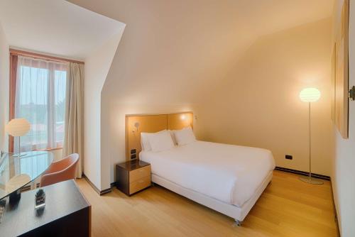 a hotel room with a white bed and a desk at NH Milano 2 Residence in Segrate