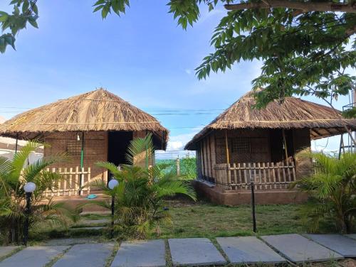 two huts with thatched roofs in a garden at Murali Guesthouse Hampi in Hampi