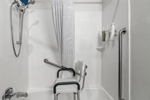 une douche dans une salle de bain blanche avec une chaise de douche dans l'établissement Spark By Hilton Merrillville, à Merrillville