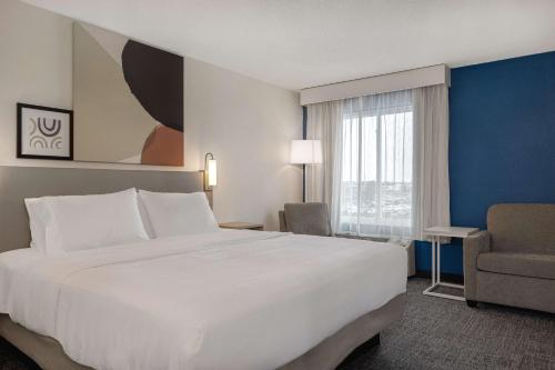 a hotel room with a large white bed and a chair at Spark By Hilton Evansville East, In in Evansville
