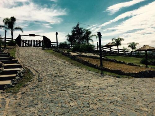 a stone road with a fence and palm trees at Cabañas Terrazas del Sol in Villa Carlos Paz