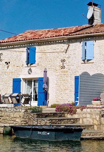 a stone house with a boat in the water at -- Charmant Gîte au Calme -- "La Maison de La Taillée aux Volets Bleus" - Bord de Rivière - Pêche - Marais Poitevin - Vendée in La Taillée