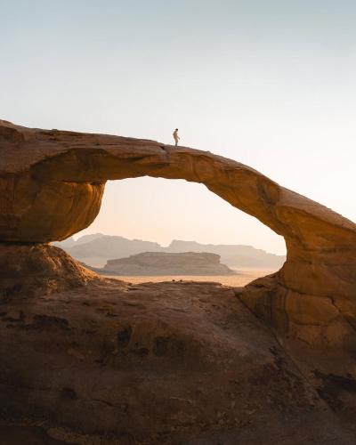 a person standing on top of an arch in the desert at Wadi Rum Quiet Desert in Wadi Rum