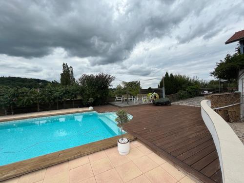 a pool with a wooden deck next to a house at Maison verdoyante et piscine in Abbans-Dessus