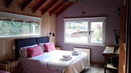 a bedroom with a bed with pink pillows and a window at Hostería Las Cumbres in Villa La Angostura