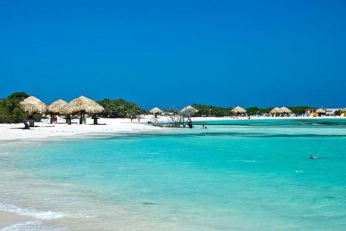 a beach with some straw umbrellas and the ocean at Aruba Sunrise Studio Near Baby Beach, San Nicolas in San Nicolas