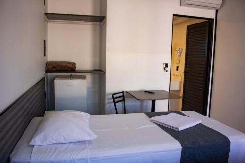a bedroom with a white bed and a table at Hotel Rosim in Pirassununga