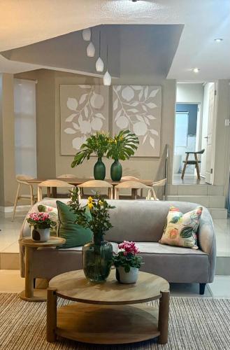a living room with a couch and tables with flowers at Wellness Guesthouse in Krugersdorp
