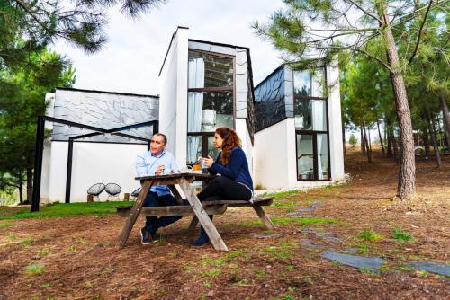 two people sitting at a picnic table in front of a house at Akassa Alojamientos Bioclimaticos en las Hurdes in Pinofranqueado