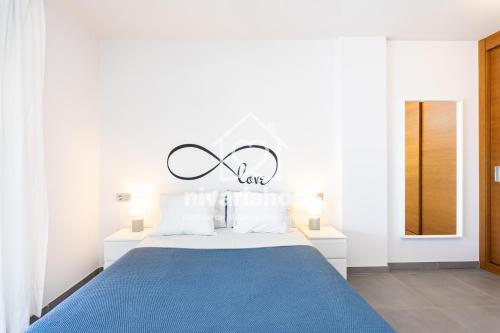 a white bedroom with a blue bed with a sign above it at The Penthouse La Tejita, by Nivariahost in La Tejita