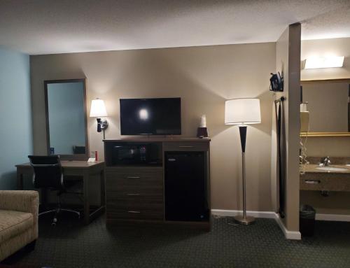 a hotel room with a desk and a tv and a room with a bed at River Hill Inn & Suites in Hudson
