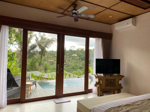 a bedroom with a bed and a television and a balcony at Micaela Bali Ubud Villas in Tegalalang