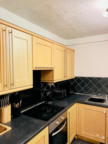 a kitchen with wooden cabinets and black counter tops at Green Woods Lovely 1 Bed Apt in Blackheath, London in London