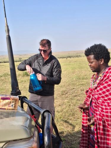 two men are standing next to a grill with a water bottle at Maasai homestay camping in Sekenani