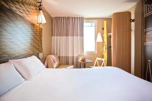 サン・ドニにあるibis Paris Saint-Denis Stade Sudの白いベッドと椅子が備わるホテルルームです。